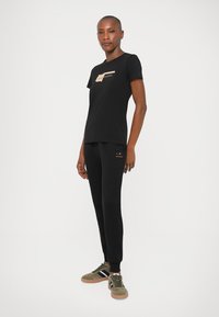 Tricou negru cu mânecă scurtă, cu un accent imprimat, asortat cu pantaloni jogger negri. Modelul poartă adidași verde măsliniu cu detalii în dungi.