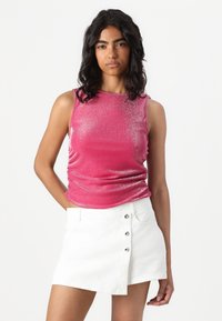Fuksia ermeløs topp med en glitrende tekstur og rynkedetaljer, kombinert med en hvit denim miniskjørt med knappdetaljer.