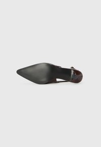 Sandal con tacco alto in pelle marrone, dalla forma affusolata, con suola nera texturizzata e una sottile cinghia, mostrata dal fondo su uno sfondo bianco.