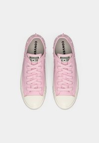 Rosa lerret sneakers med pigger langs sidene, hvit gummitåhette og såle, samt flate rosa snørebånd. "Converse All Star"-logo synlig.