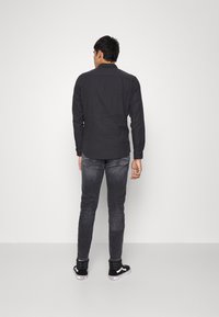 Camisa negra de manga larga con cuello, combinada con jeans gris oscuro y zapatillas negras. La camisa tiene una textura de tela suave y un corte estándar.