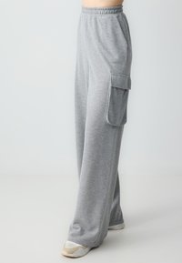 Graue Sweatpants aus weichem Stoff, mit elastischem Bund, Seitentaschen und einer großen Cargo-Tasche am Oberschenkel.