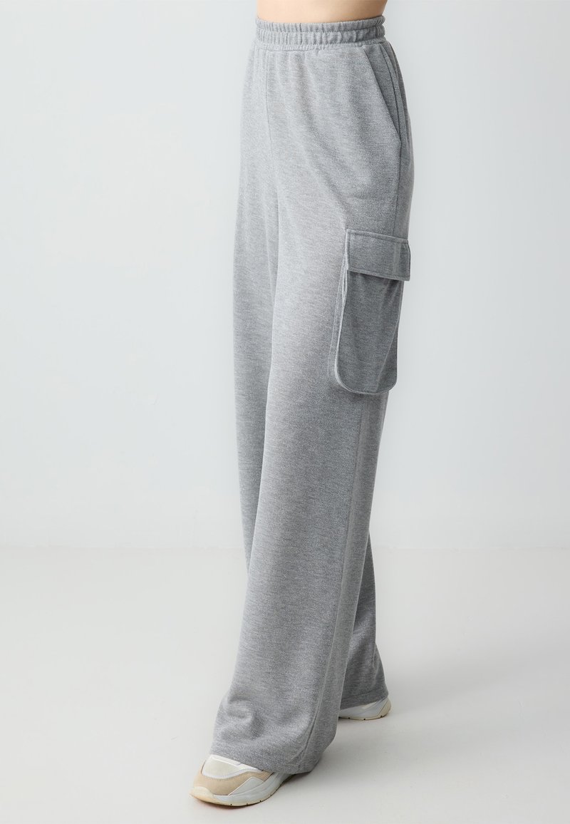Graue Sweatpants aus weichem Stoff, mit elastischem Bund, Seitentaschen und einer großen Cargo-Tasche am Oberschenkel.