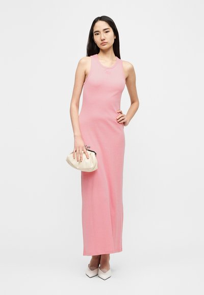 Ροζ μάξι φόρεμα χωρίς μανίκια με εφαρμοστή σιλουέτα, κατασκευασμένο από πλεκτό ύφασμα. Συνδυασμένο με κρεμ τσάντα φάκελο και λευκές μυτερές γόβες.