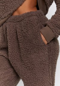 Brun fleece loungewear sæt med blødt, tekstureret stof, elastisk talje og ribbede manchetter; inkluderer sidelommer for ekstra bekvemmelighed.