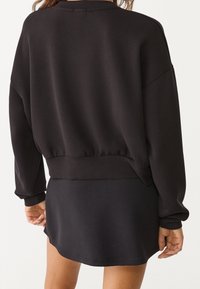 Sudadera negra con hombros caídos y dobladillo fruncido, combinada con una minifalda negra. Textura suave, diseño simple sin patrones.