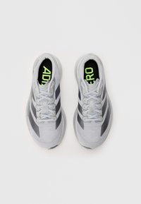 Baskets de sport grises claires avec des accents et des lacets noirs, présentant un dessus texturé et un logo vert sur la semelle intérieure.