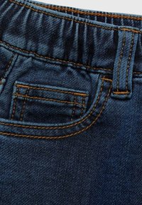Mörkblå denimtyg med en elastisk midja, synlig sömnad i en kontrasterande orange färg och en liten frampocketdetalj.