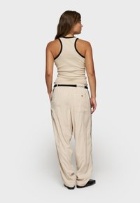 Top sin mangas beige con ribetes negros y pantalones beige holgados. Los pantalones tienen un bolsillo trasero y una cinturilla negra con una etiqueta de marca.