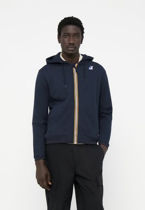 Marineblå zip-up hettejakke laget av bomullsmiks, med stripete glidelås, justerbar hette og ribbestrikkede mansjetter. Logo-patch på brystet.