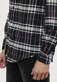 Zwart-wit geruite flanellen overhemd met paarse accenten, voorzien van knoopsluiting en een label aan de zoom. Textuurstof, casual ontwerp.