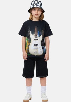 Schwarzes T-Shirt mit einem Motiv von mehreren E-Gitarren in verschiedenen Farben. Getragen mit schwarzen Shorts, weißen Socken, Sneakers und einem karierter Fischerhut.