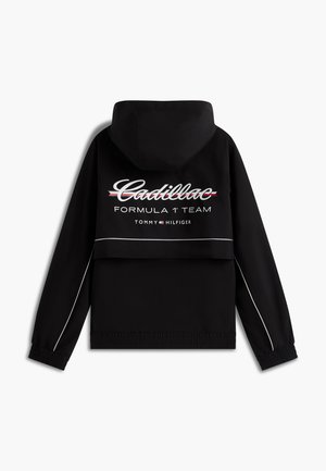 Fekete kapucnis dzseki "Cadillac Formula 1 Team Tommy Hilfiger" felirattal és logóval a háton, fehér csíkozással az ujjakon és az alján.