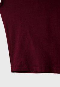 Gros plan sur un tissu marron montrant une texture lisse et une couture d'ourlet sur un vêtement, sur un fond clair uni.