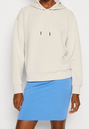 Felpa beige con cappuccio, cordini e logo, abbinata a una gonna aderente di un blu chiaro. Tessuto morbido, design casual e stile semplice.