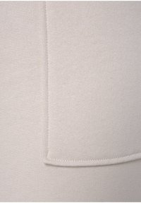 Hellbeige Strickstoff mit glatter Textur, horizontalen Linien und einem kontrastierenden aufgenähten Taschen-Detail.