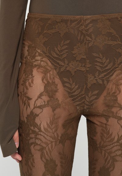 Brune blondeleggings med blomsterprint og en semi-gjennomsiktig design, kombinert med en tettsittende mørk topp. Teksturert blondes utvikling kontrasterer med jevnt materiale.