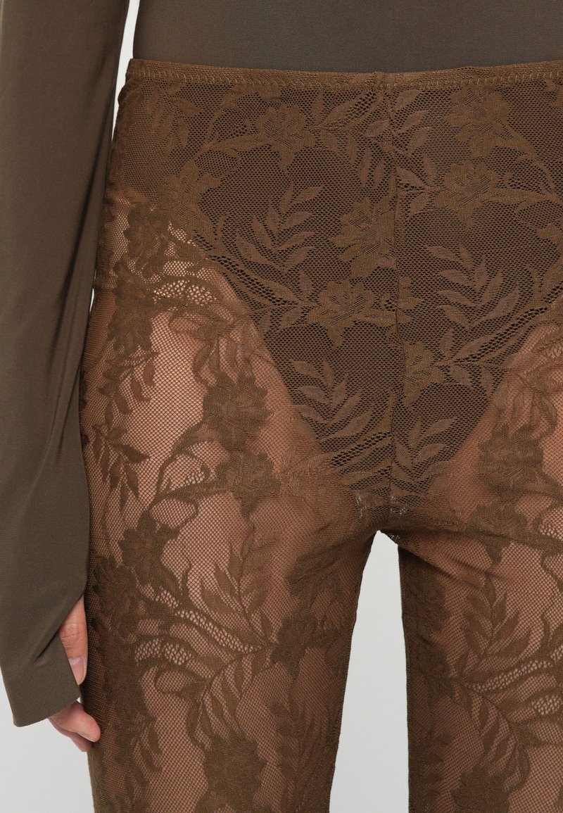 Braune Spitzenleggings mit floralen Mustern und semi-transparentem Design, kombiniert mit einem figurbetonten dunklen Oberteil. Texturierte Spitze kontrastiert mit glattem Material.