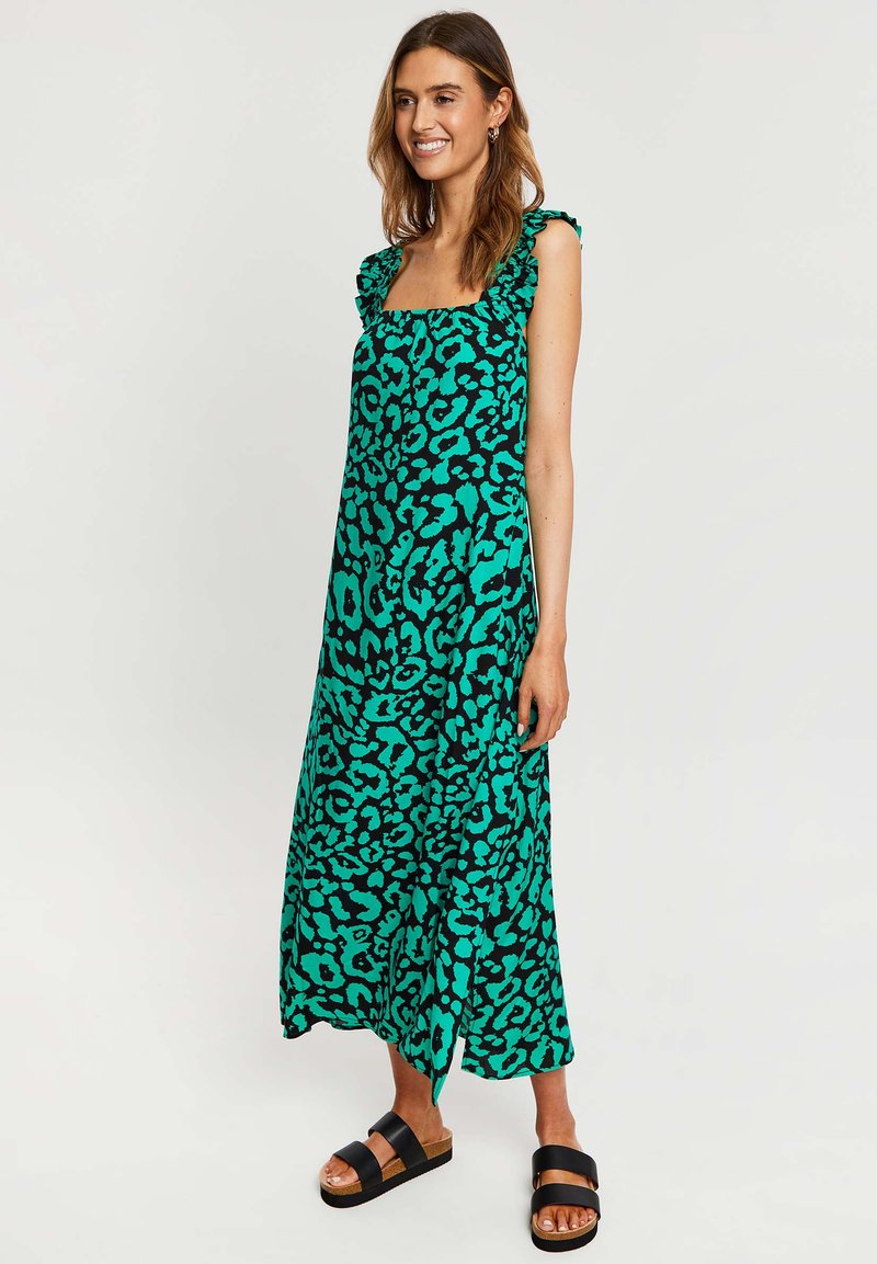 Maxikleid mit grünem Leopardenmuster, Rüsche-Trägern, quadratischem Ausschnitt und fließender Silhouette. Kombiniert mit schwarzen Slidesandalen.