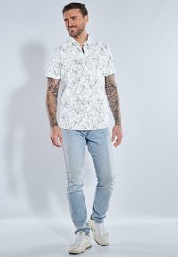 Kurzärmliges weißes Hemd mit floralem Schwarzumriss-Muster, kombiniert mit hellblauen destroyed Jeans und weißen Sneakers.