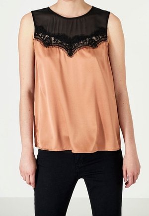 Top sans manches en satin pêche avec empiècement noir transparent et bordure en dentelle, porté avec un pantalon noir, visible des épaules aux hanches.