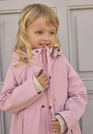 Giacca impermeabile rosa con cappuccio, dotata di cerniera frontale, polsini elasticizzati e orlo svasato. Il modello ha capelli lunghi e mossi e sorride.