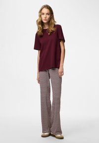 Vinrød bomulds T-shirt parret med cremefarvede og vinrøde stribede bukser med vide ben; båret med beige slip-on sko. Glat tekstur.