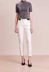 Haut gris à manches courtes avec un subtil éclat, associé à un pantalon blanc sur mesure et des talons noirs, présentant un détail de taille contrastant.