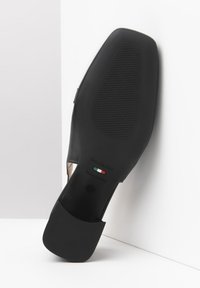 Scarpa in pelle nera con una superficie liscia, tacco basso e suola in gomma dotata di un battistrada decorato e etichetta con il marchio. Prodotta in Italia.