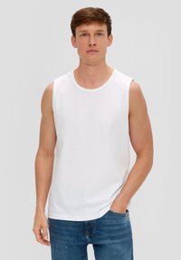 Weißes ärmelloses Shirt aus weicher Baumwolle, mit rundem Halsausschnitt und geradem Saum. Kombiniert mit blauen Jeans steht das Modell frontal.