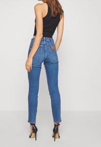 Smala jeans i medelblå denim med hög midja, med bakfickor och en läderetikett, parat med svarta högklackade skor.