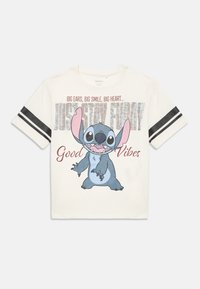 Camiseta blanca de manga corta con rayas negras en las mangas, que presenta al divertido personaje de dibujos animados Stitch sonriendo y el texto "Grandes orejas, gran sonrisa, gran corazón... Solo mantén el humor, buenas vibras."