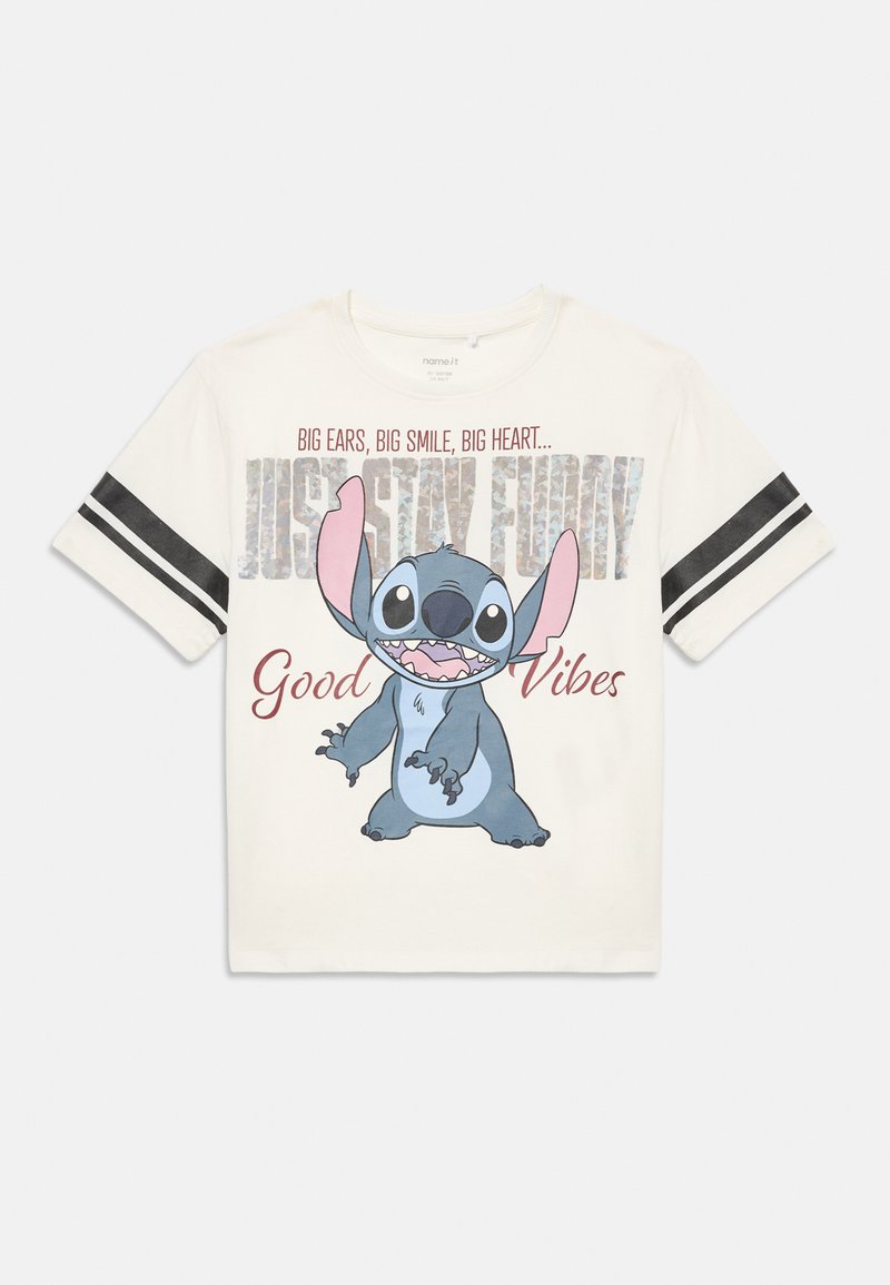 Camiseta blanca de manga corta con rayas negras en las mangas, que presenta al divertido personaje de dibujos animados Stitch sonriendo y el texto "Grandes orejas, gran sonrisa, gran corazón... Solo mantén el humor, buenas vibras."