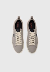 Gray canvas sneakers with cream-colored laces, rubber sole, and a rear pull tab. Features "Hugo" branding on the tongue and insole.