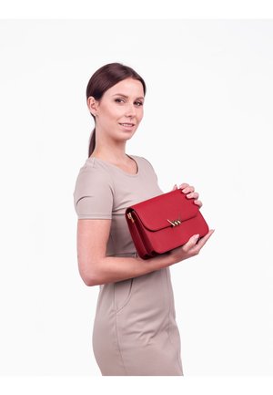 Rote Lederhandtasche mit einem Klappenverschluss und goldfarbenen Beschlägen. Die Tasche hat eine glatte Textur und eine strukturierte Form, gehalten von einem Model.