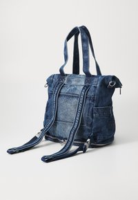 Denim bevásárlószatyor dupla füllel, cipzáros záródással és állítható pántokkal. Jellemzője a textúrált anyag és a kontrasztos varrási részletek.