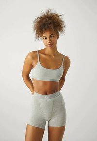 Lys grå sportbh og shorts-sett med UGG-merke på livlinjen. Stoffet ser glatt ut med et stramt, fleksibelt design.