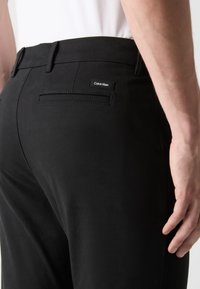 Schwarze Hose aus glattem Stoff mit geradem Schnitt, Gesäßtasche mit dezentem Stickakzent und einem Calvin Klein Logoetikett.