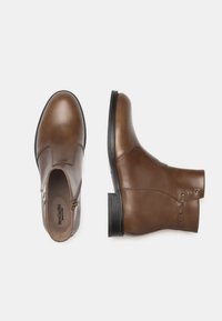 Stivali alla caviglia in pelle marrone con punta tonda, zip laterale e borchie decorative. Presentano una suola in gomma piatta e una texture liscia.