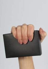 Schwarze rechteckige Box, die in einer Hand mit ordentlich manikürten, hellrosa Nägeln gehalten wird. Glatte, matte Oberfläche; minimalistisches Design mit scharfen Kanten.