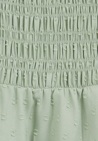 Šviesiai žalias audinys pasižymi klostytu, tekstūruotu dizainu su subtiliais pakeltais taškais visame paviršiuje. Sklandus paviršius su surinktomis sekcijomis.