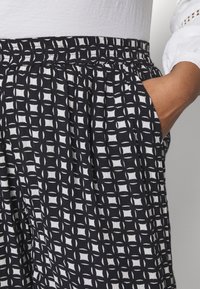 Zwart-witte gestreepte broek met een elastische tailleband, voorzien van zijzakken en een lichtgewicht stof. Ruitvormig ontwerp met een gestructureerde afwerking.