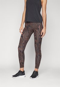 Leggings marron et noirs à motifs avec une coupe ajust�ée, associés à un débardeur noir ample et des chaussures de sport noires.