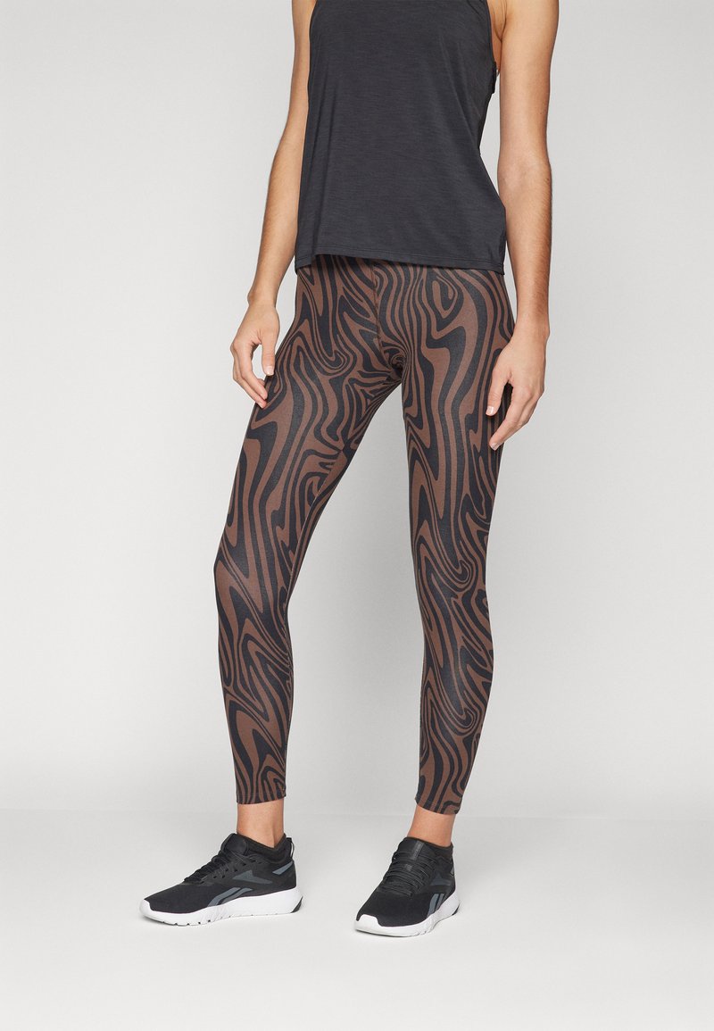 Leggings marron et noirs à motifs avec une coupe ajustée, associés à un débardeur noir ample et des chaussures de sport noires.