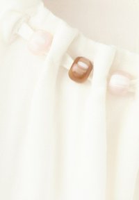Gros plan sur un tissu blanc avec des plis décoratifs maintenus par des perles rondes translucides de couleurs rose pâle et marron.