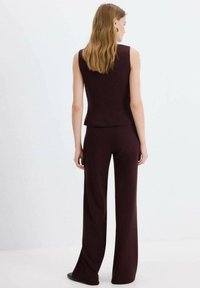 Costum bordo în două piese, cu un top mulat fără mâneci și pantaloni cu picioare largi, confecționat dintr-un material neted și texturat. Fără accente vizibile.