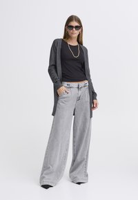 Pilkas kardiganas dėvimas virš juodos palaidinės, derinamas su platėjantys pilkais džinsais. Aksesuarai: juodi saulės akiniai ir perlų vėrinys.