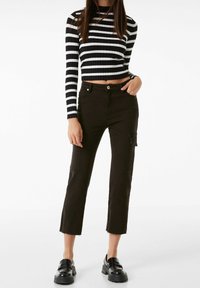 Svart och vit randig ribbad cropped topp med långa ärmar, i kombination med högmidjade mörka cargobyxor med fickor och råa fållar.