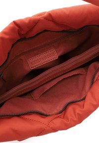 Quilted red fabric handbag interior with a zipper pocket and a label tag. Smooth texture with structured compartments for organization.