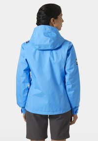 Blauwe waterdichte jas met capuchon, voorzien van een matte afwerking, verstelbare manchetten en een logodetail op de linkermouw.